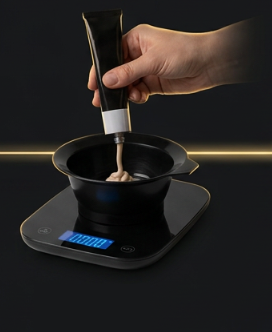 Hand dispensing hair color into a bowl on the QUE scale